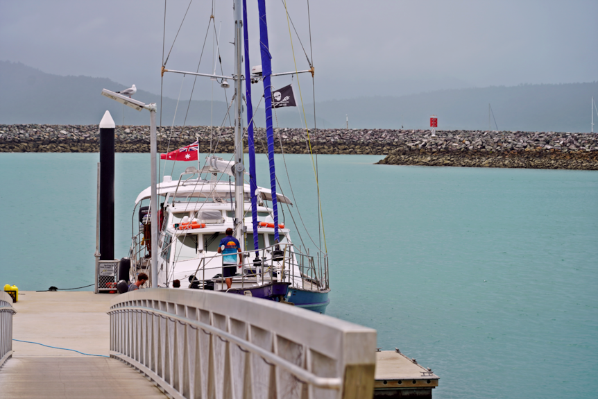 A yacht at a dock, with water and a rock seawall visible behind it