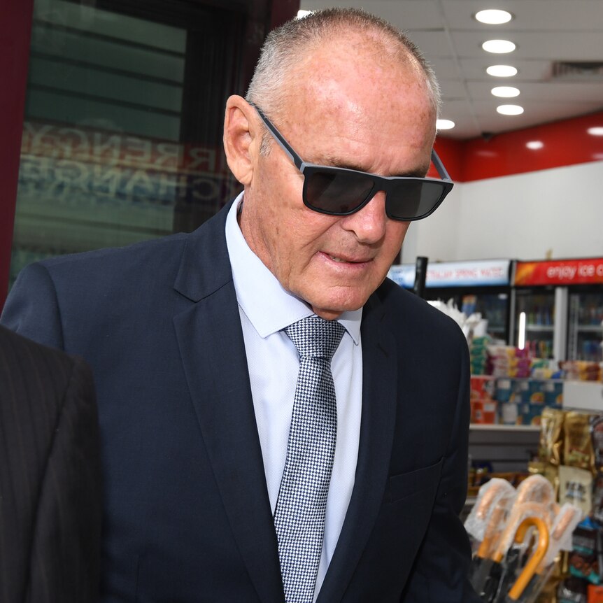A man wearing dark glasses walking outdoors with his head bowed.