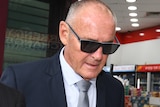 A man wearing dark glasses walking outdoors with his head bowed.