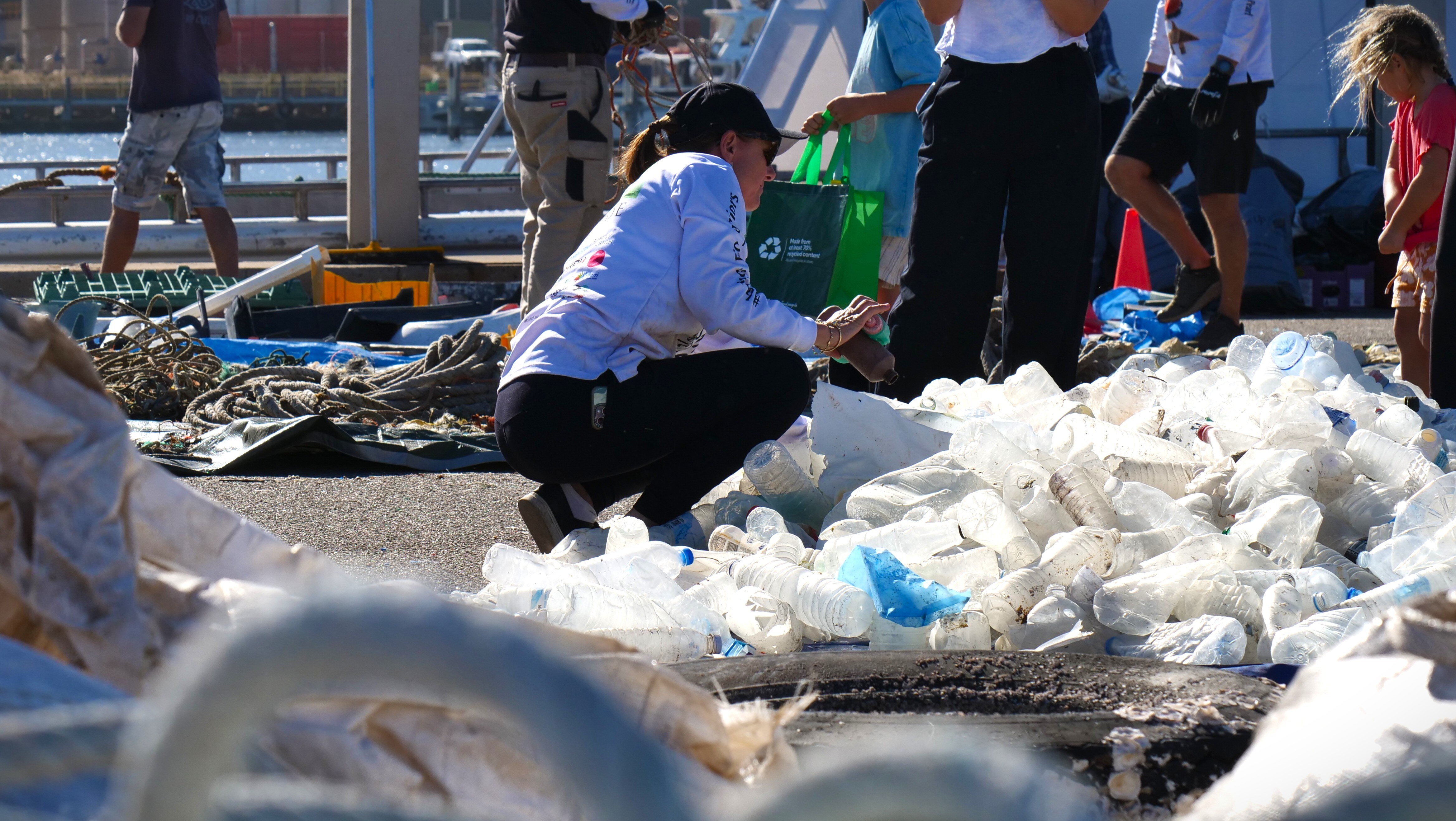 A woman looks over a large pile of plastic bottles on the ground 