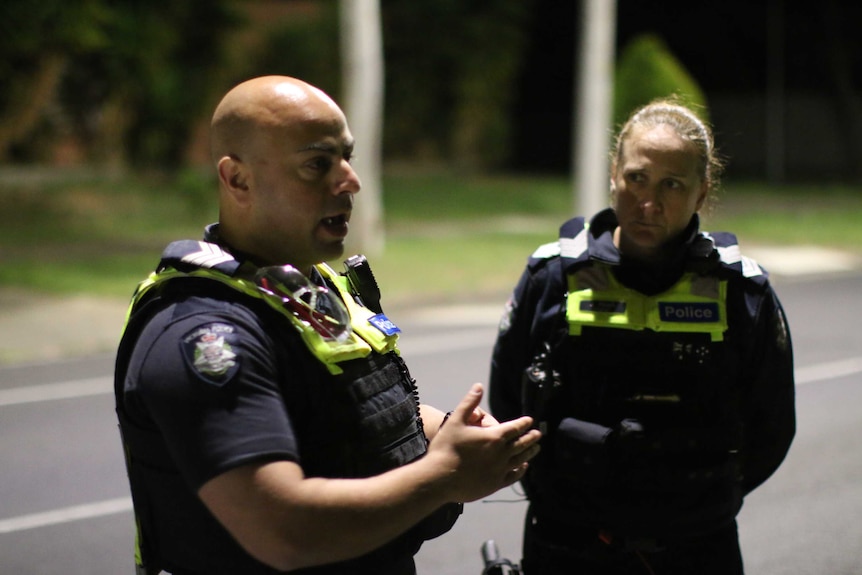 A male and a female police officer speaking to each other in a suburban street.