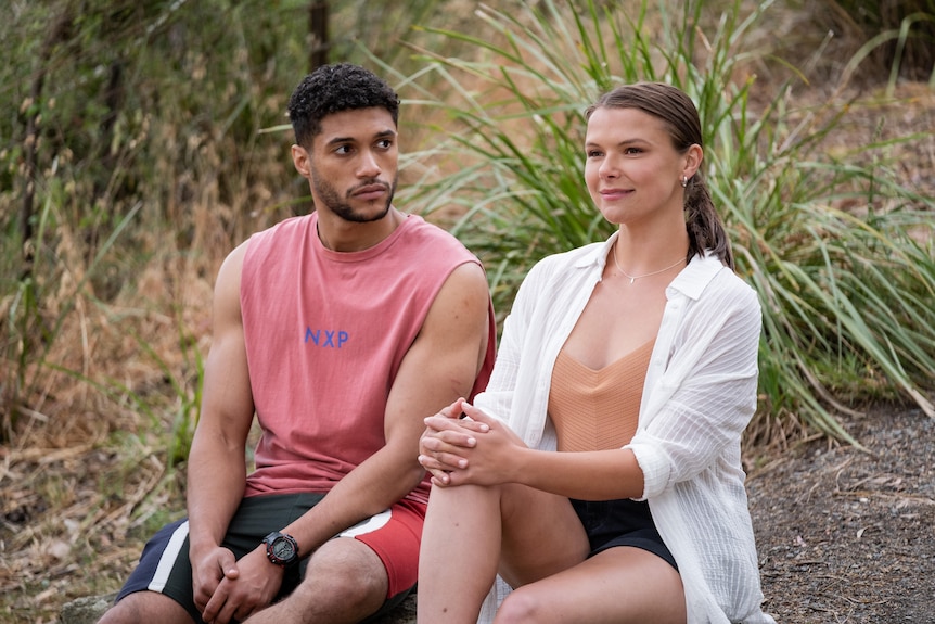 A young man and a young woman sit outside in a scene from a TV show.