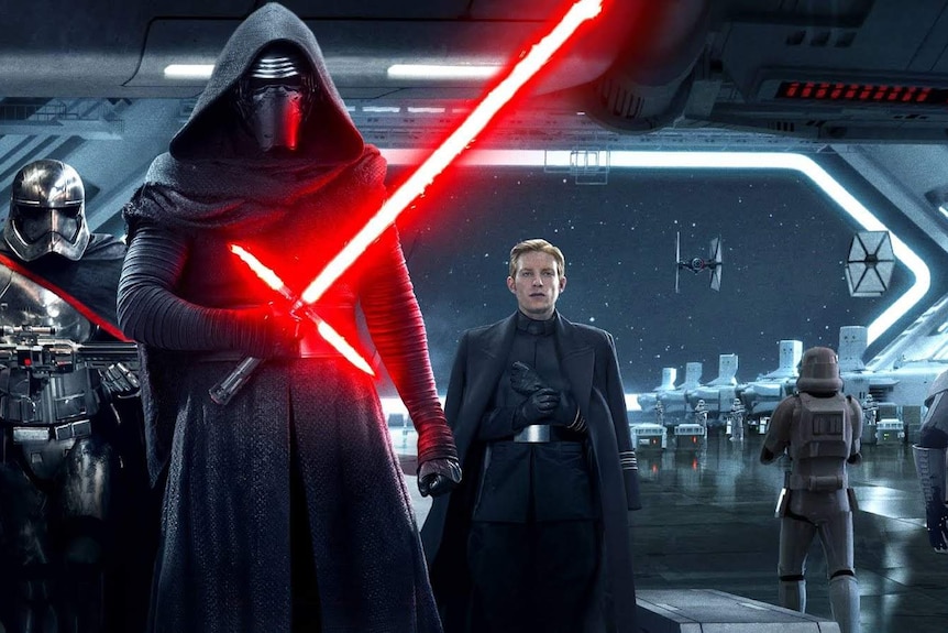 Kylo Ren dressed in black holds a red lightsabre while standing in a spaceship, flanked by two henchman.