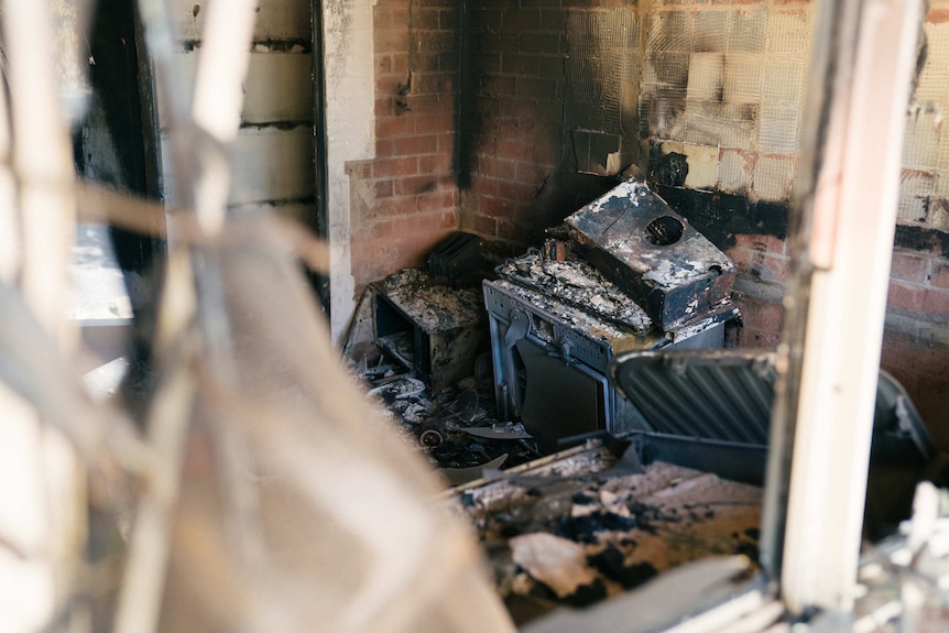 An oven or possibly a washing machine lies burnt and melted up against a wall.