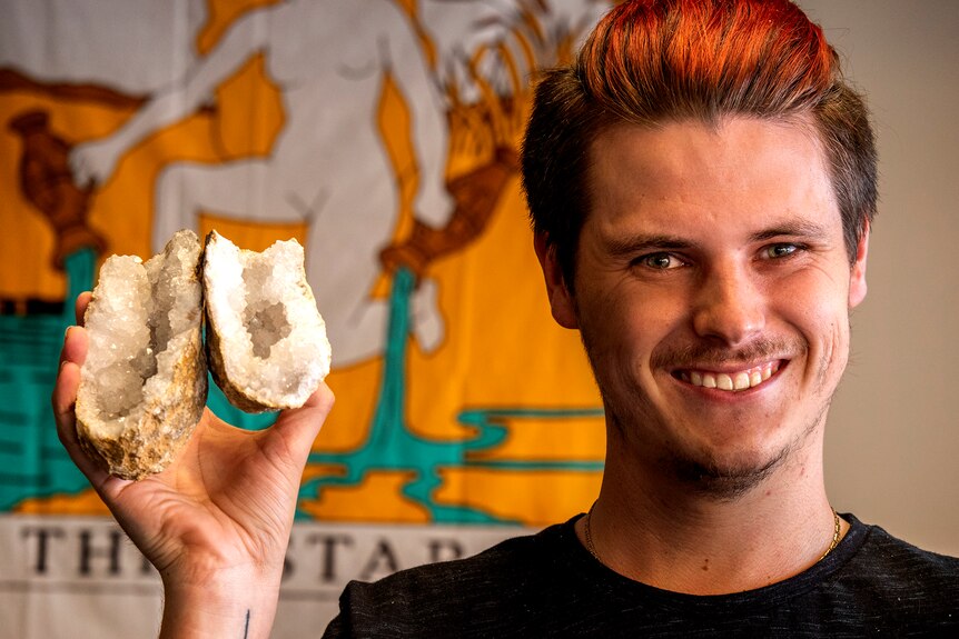 A man holds a geode cracked open revealing crystals.