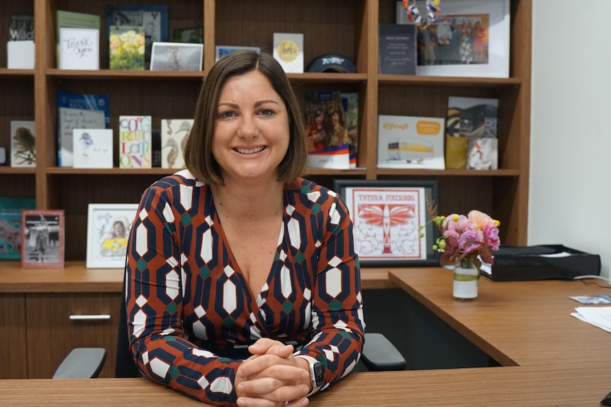 A woman in a dress smiling at the camera, seated in an office.