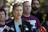 Sally McManus speaks passionately behind a host of media microphones with people in union shirts in the background