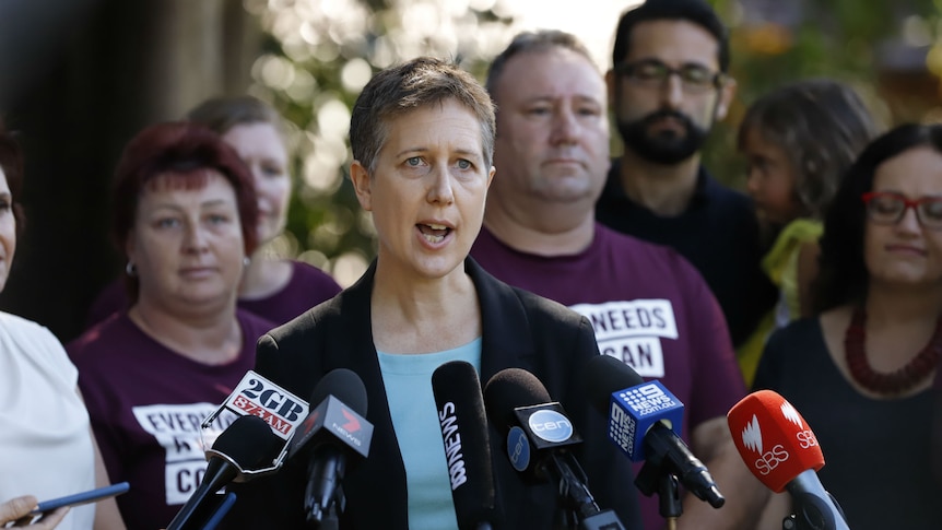 Sally McManus speaks passionately behind a host of media microphones with people in union shirts in the background