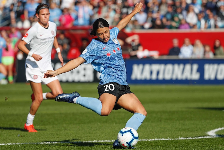 Sam Kerr leans back with her arms outstretched as she prepares to shoot with her right foot