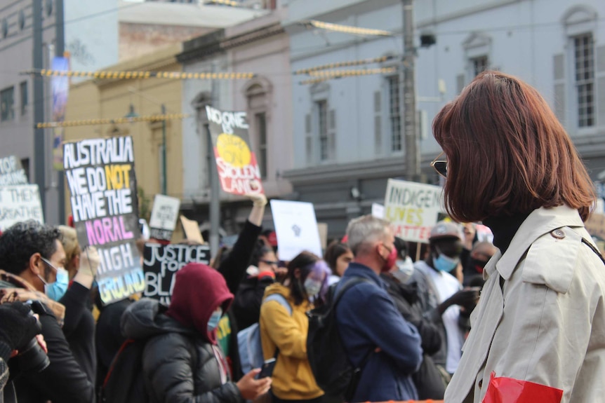 An unidentified woman at a protest, with people holding anti-racism signs behind her.