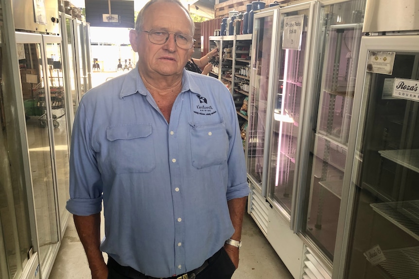 a man with his hands in his pocket standing in a room with fridges looks at the camera