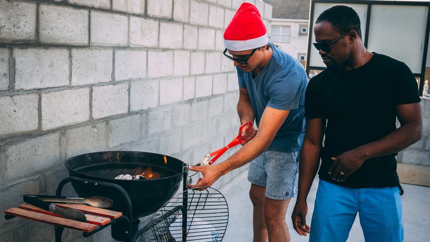 Two men stand at barbecue at Christmas for a story about the work women do at Christmas