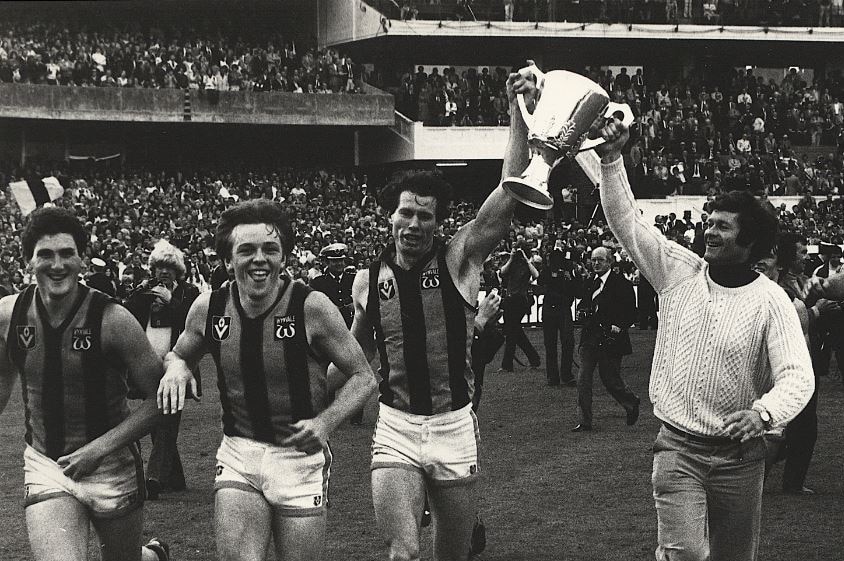 Don Scott carries the 1978 Premiership Cup with coach David Parkin, while teammates smile and the crowd looks on.