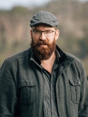 A bearded man wears a beret and jacket.