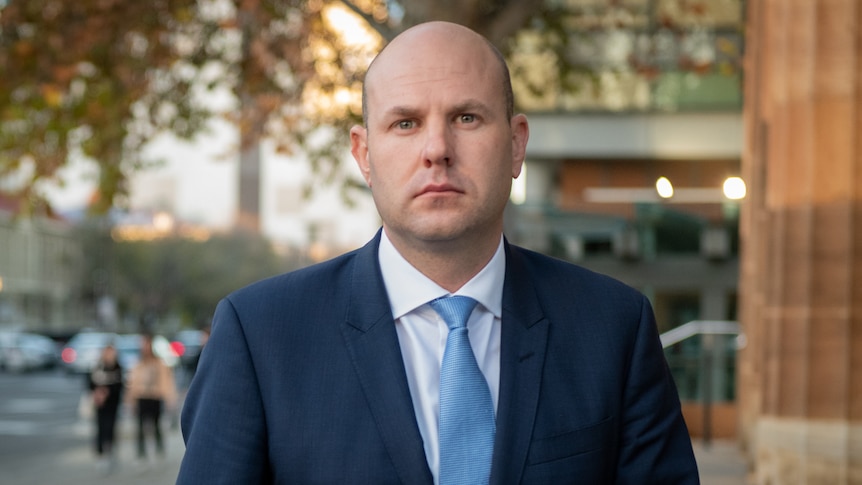 A man wearing a dark blue suit and a light blue tie