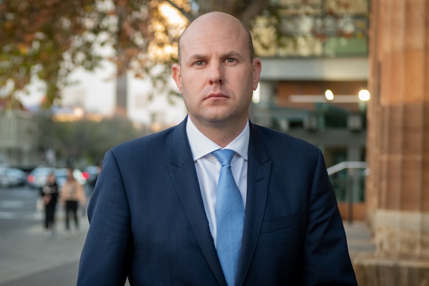 A man wearing a dark blue suit and a light blue tie