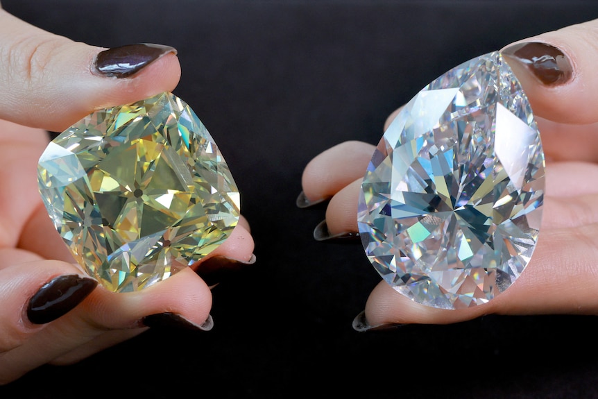 Hands hold two large diamonds side by side