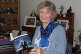 Lesley Mooney sits at a dining table holding a book open