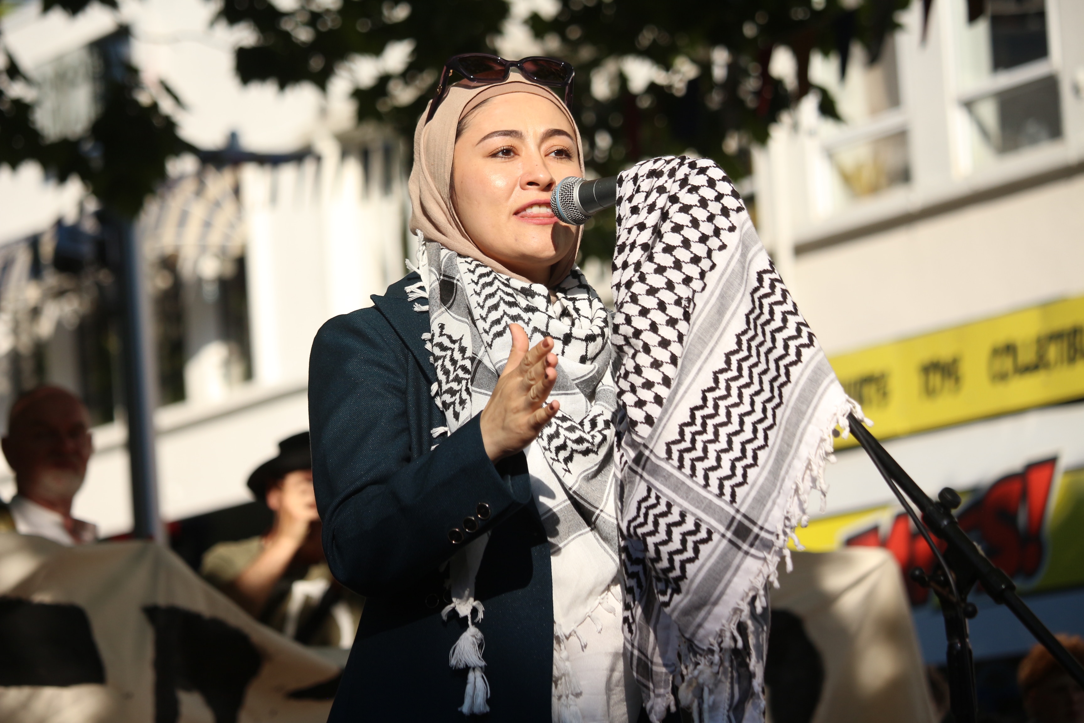 Fatima Payman viste bufandas y una chaqueta y habla por un micrófono en un mitin.