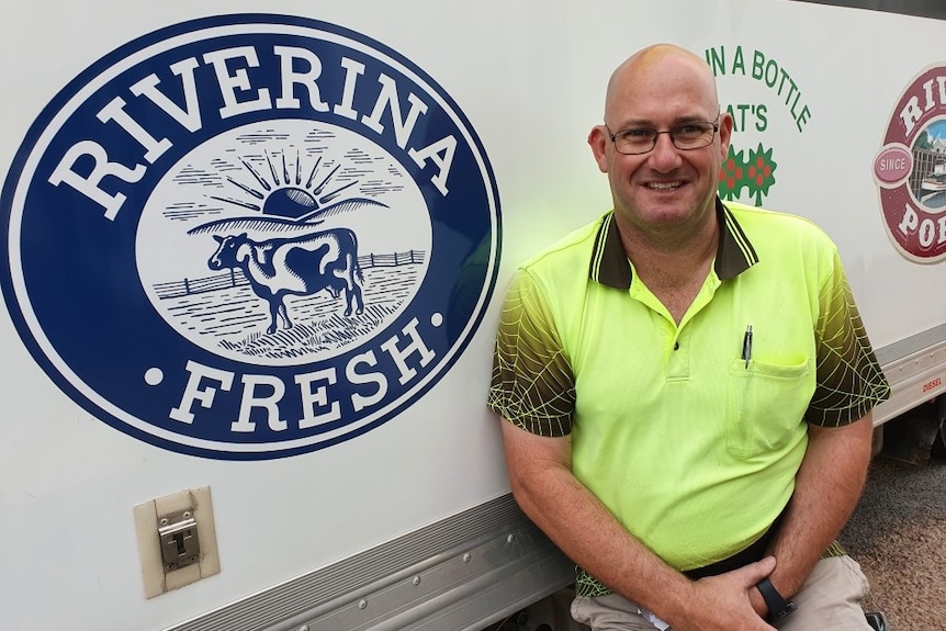 Bald man with glasses sits in front of a refrigerated truck with a 'Riverina Fresh' logo on the side of it.