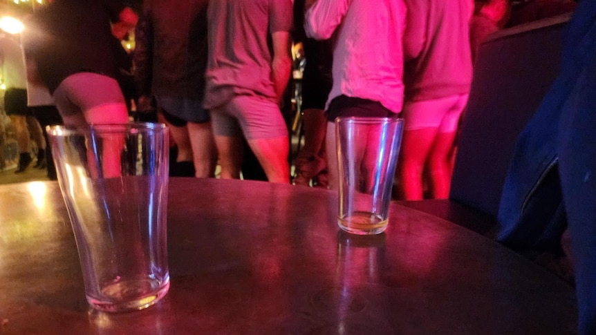two empty beer glasses on table in foreground and men with their pants down revealing underwear in background