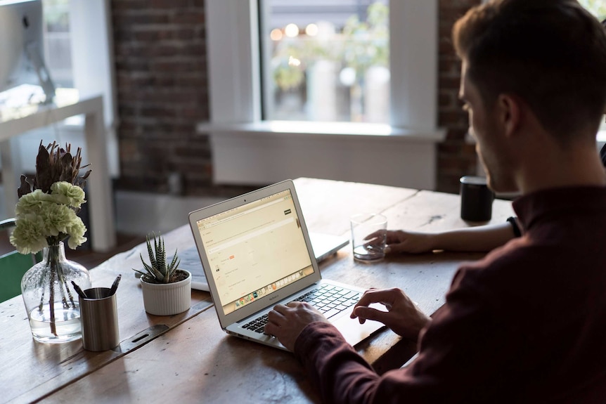 A man works on a laptop on a bench.