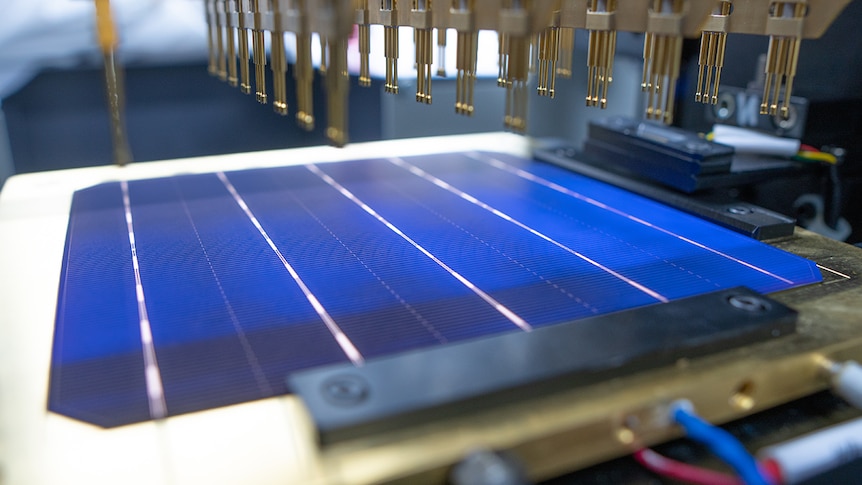 A solar cell being tested with machinery over a blue solar cell.