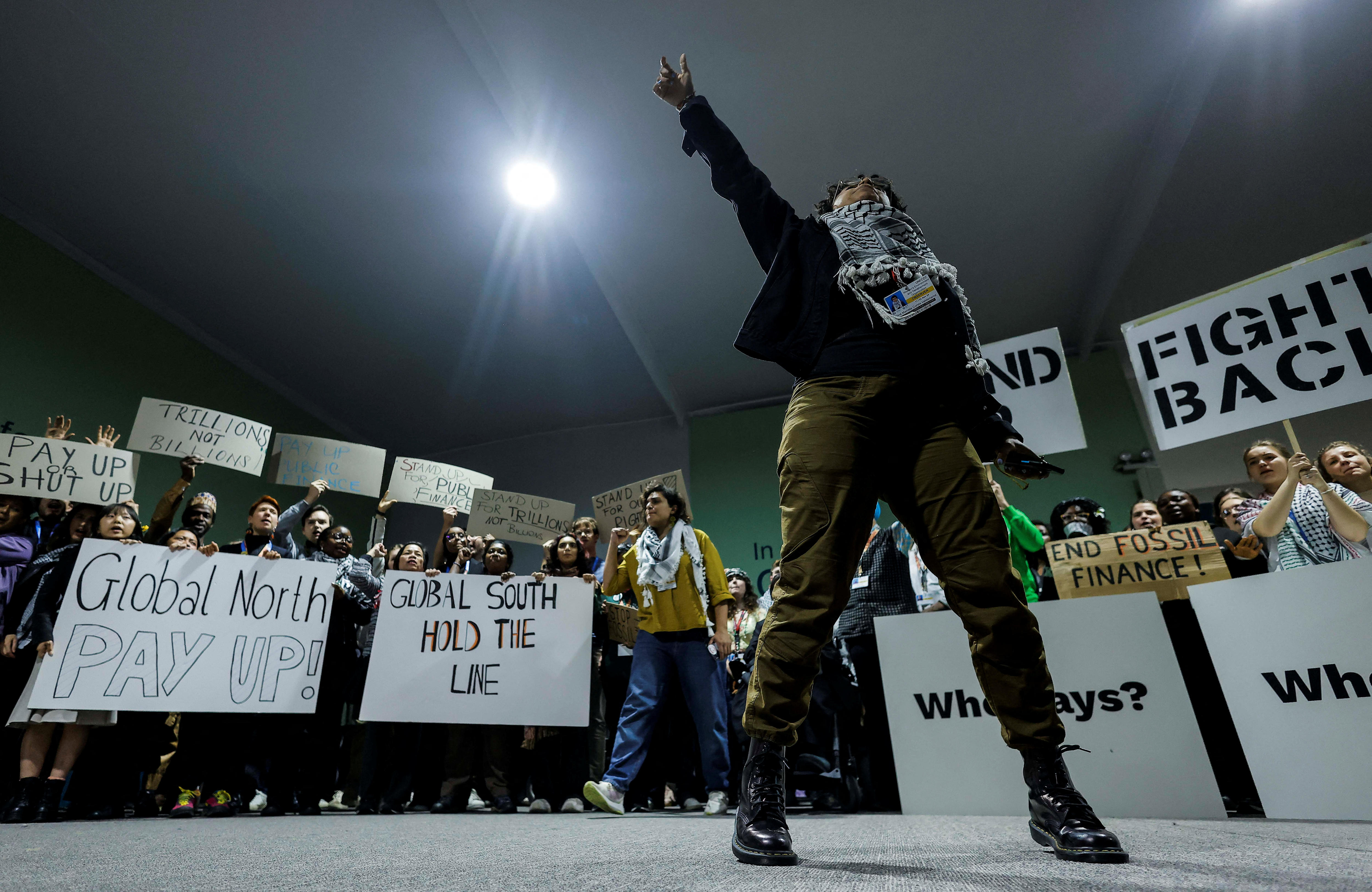A crowd of activists holding white protest placards wite one person dressed in black, centre, pointing upwards
