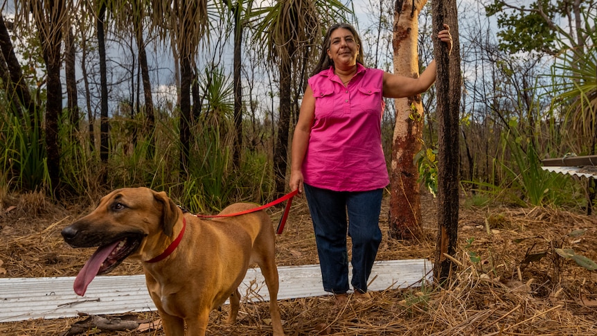 Pauline Cass stands with her dog, next to burnt out trees, on her property in Humpty Doo.