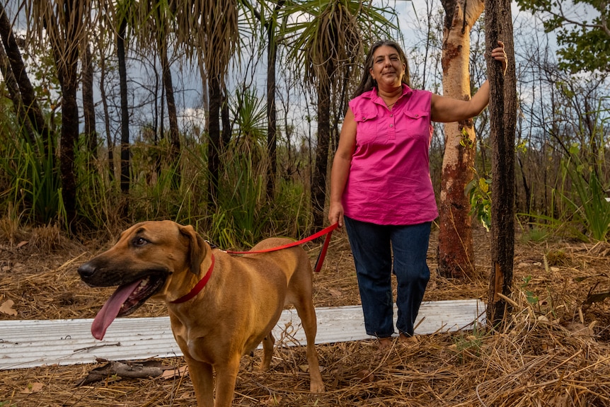 Pauline Cass stands with her dog, next to burnt out trees, on her property in Humpty Doo.
