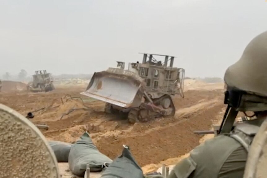 A soldier in a tank looking at a bulldozer ahead