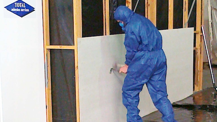 As part of an awareness campaign, a worker displays a method of removing asbestos safely