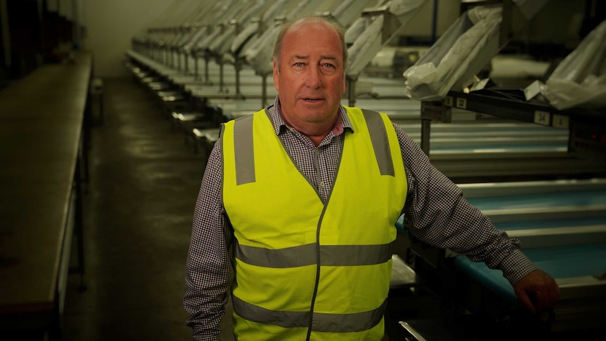 A middle aged man standing in an empty cherry packing room wearing a yellow protective vest looking at the camera.
