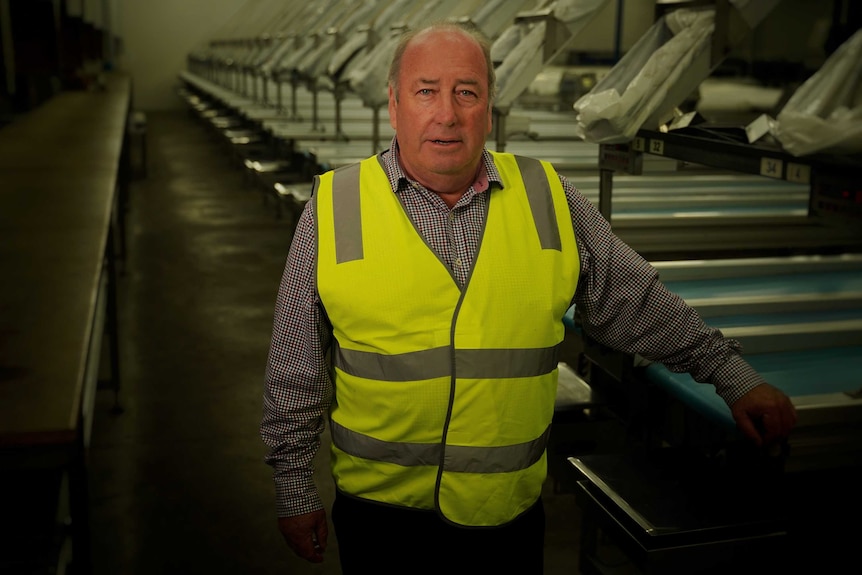 A middle aged man standing in an empty cherry packing room wearing a yellow protective vest looking at the camera.