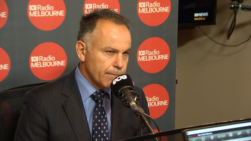 A man in a suit sits behind an ABC microphone at ABC Radio Melbourne