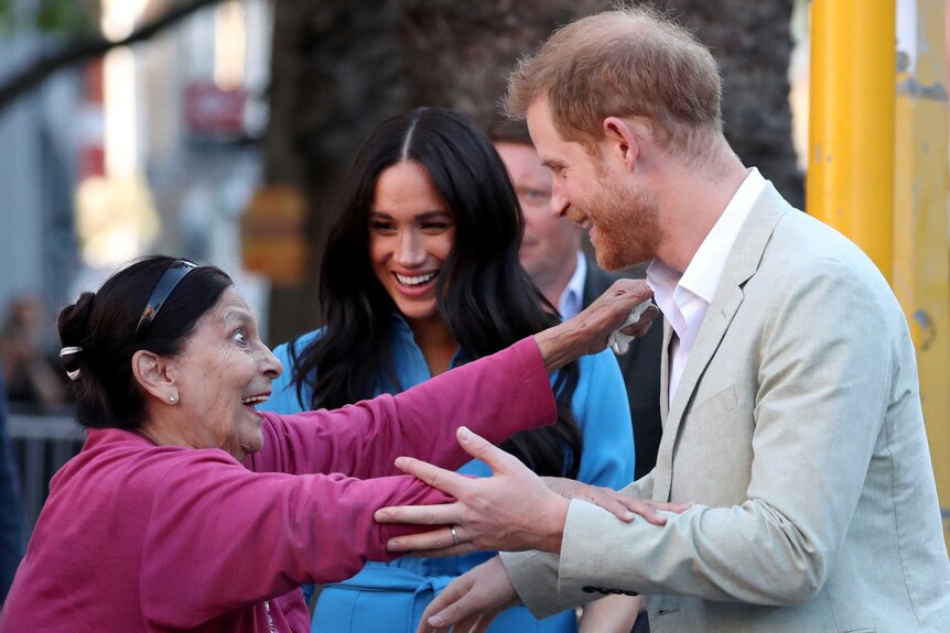 Britain's Prince Harry and Meghan greet an elderly woman who has her arms our to hug Harry