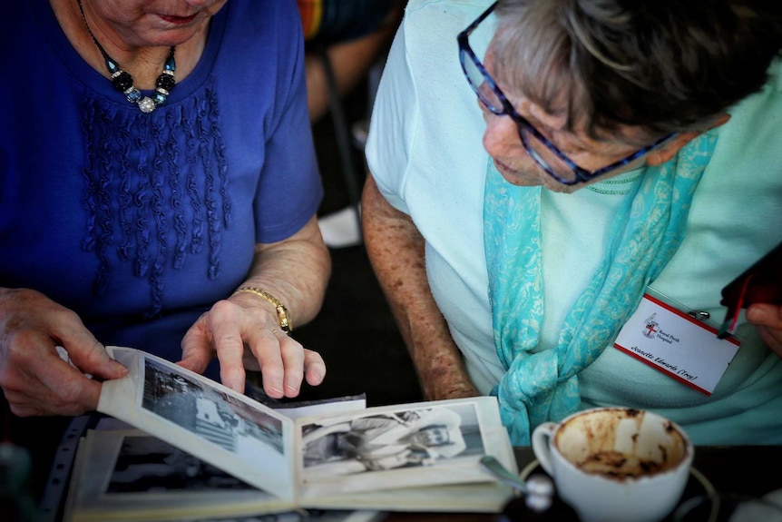 A close-up shot of two older women looking closely at black and white photos in photo albums.