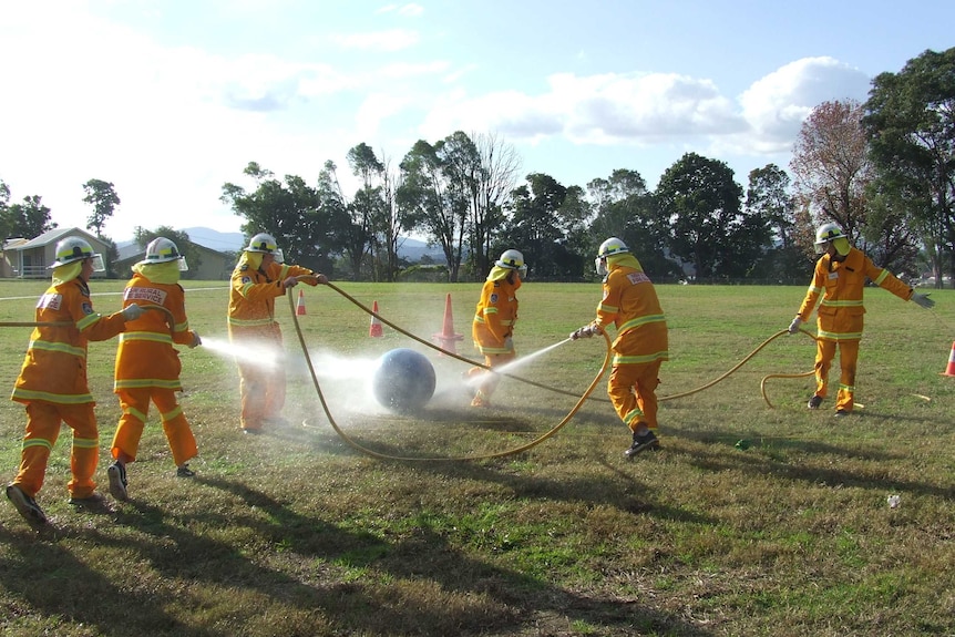 Firefighting cadets in full uniform running around with hoses during practical test.