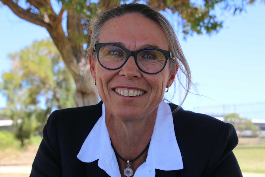 A woman in a suit smiles at the camera while in a park