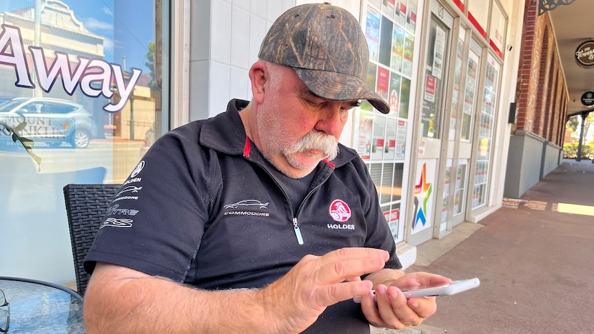 A man looks down at mobile phone on city street.