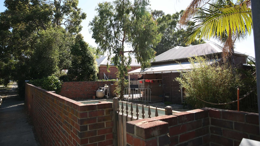 The front yard of a tin roof and brick house. Trees and a bbq in the yard.