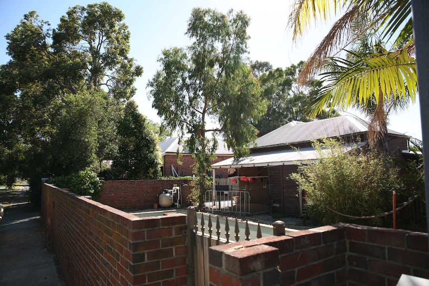 The front yard of a tin roof and brick house. Trees and a bbq in the yard.