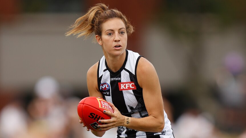 A Collingwood AFLW player holds the ball in two hands during a match.