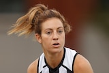 A Collingwood AFLW player holds the ball in two hands during a match.