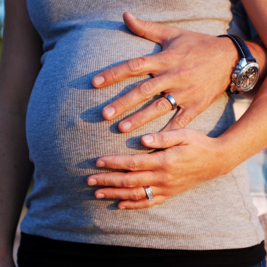 A man and woman's hands cradle the woman's pregnant belly.