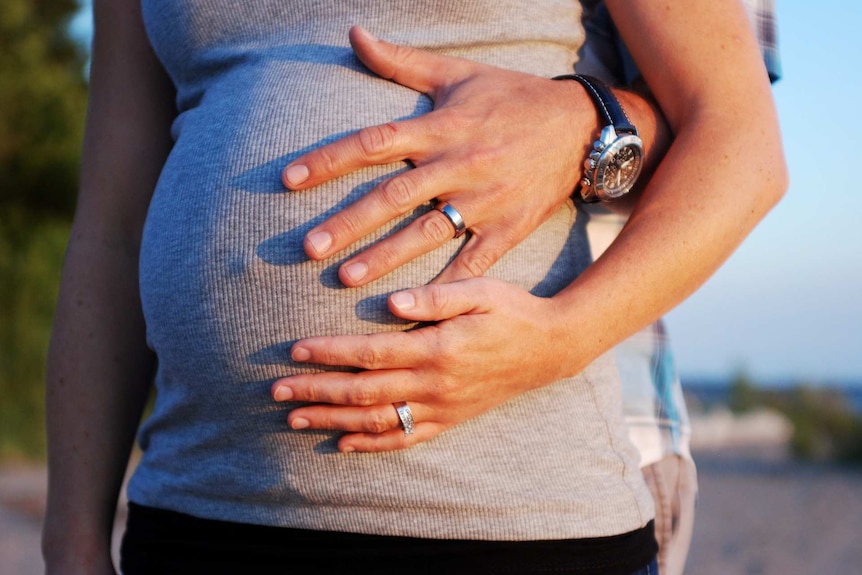 A man and woman's hands cradle the woman's pregnant belly.