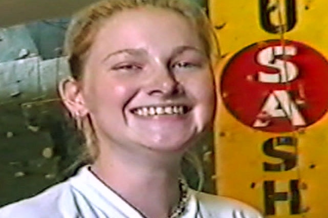 Anj Barker smiling as a 16-year-old in front of a sign.