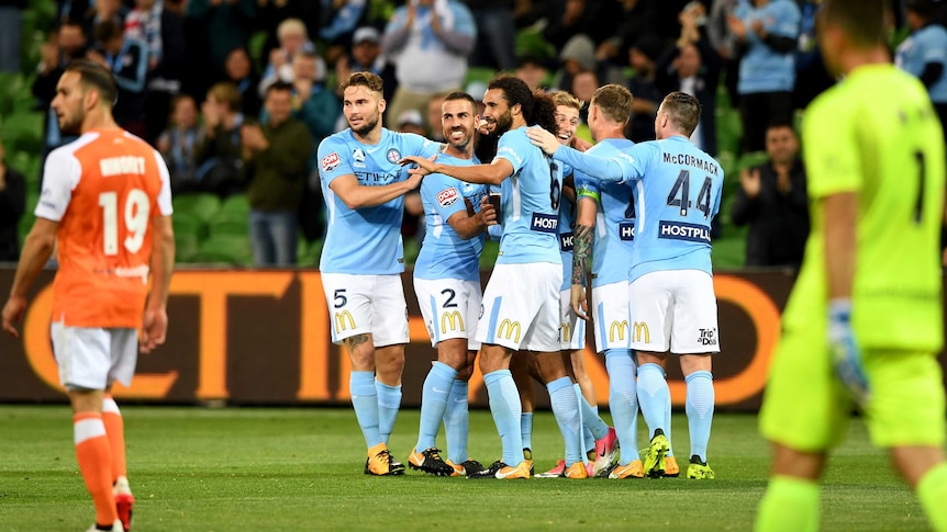 Melbourne City players celebrate with sad Roar players in the foreground.