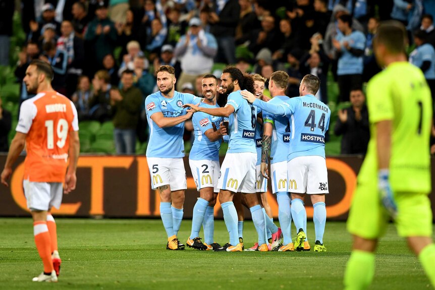 Melbourne City players celebrate with sad Roar players in the foreground.