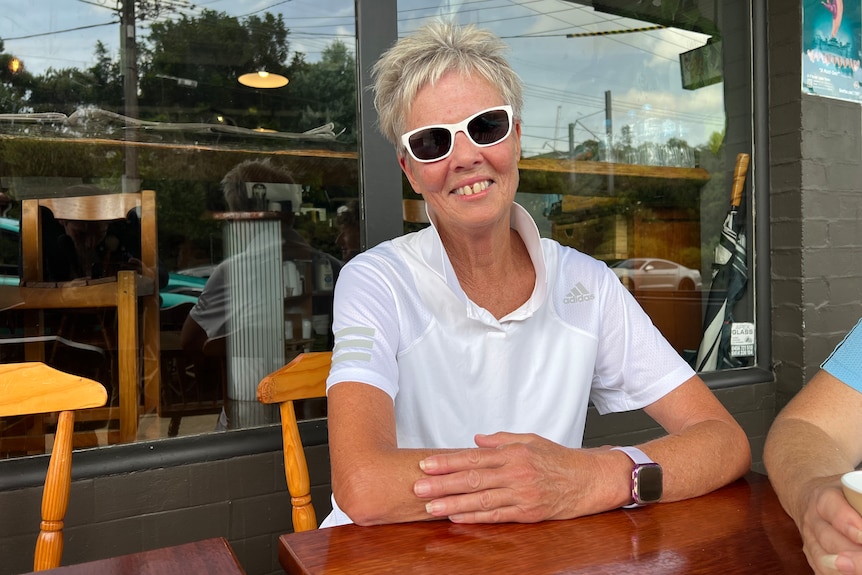 Belinda Harrison sentada al aire libre en un café con gafas oscuras y sonriendo 